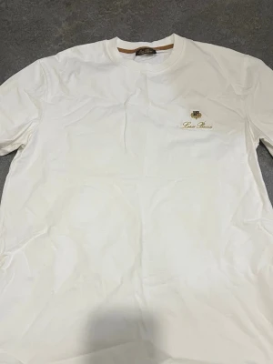 Vit t-shirt från Lord Benson - Vit t-shirt från Lord Benson med rund halsringning och broderad logga samt text på bröstet. Klassisk och stilren design som passar till många olika outfits. Tillverkad i mjuk bomull för en bekväm känsla hela dagen.