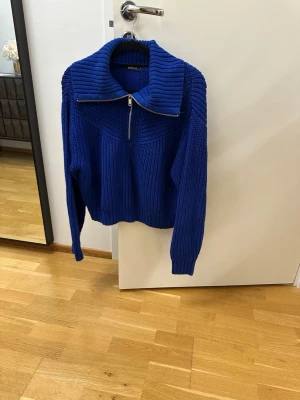 Kornblå stickad tröja med dragkedja - Säljer en kornblå stickad tröja med hög krage och dragkedja framtill. Tröjan har grovstickad struktur, långa ärmar och ribbade muddar. Perfekt för dig som gillar en avslappnad men ändå trendig look.