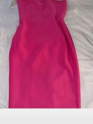 Rosa one shoulder klänning - Snygg rosa klänning med one shoulder-design och dekorativa pärlor längs axeln. Klänningen har en figurnära passform och är perfekt för dig som vill sticka ut. Materialet känns mjukt och följsamt.