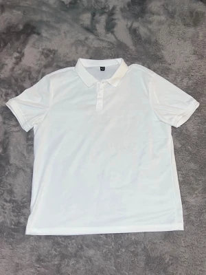 Vit pikétröja med krage - Klassisk vit pikétröja med krage och korta ärmar. Tröjan har knappar framtill och är tillverkad i ett mjukt material som känns skönt mot huden.  Längd 71cm