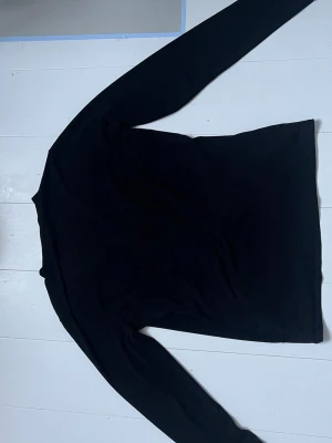 Svart långärmad tröja - En enkel svart långärmad tröja med rund hals. Tröjan har en rak passform och är tillverkad i ett mjukt material som passar perfekt till lager-på-lager. Stilren och lätt att matcha med olika outfits.