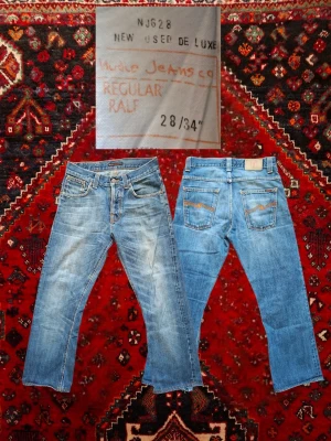Ljusblå Nudie Jeans Regular Ralf - Säljer ett par ljusblå jeans från Nudie Jeans Co, modellen Regular Ralf. Klassisk femficksmodell med raka ben och snygga slitningar framtill. Jeansen har kontrastsömmar och patch bak i midjan. Tillverkade i 100% bomull för en skön känsla. Sitter som w29, mått kan ges ut vid behov. Priset kan gå ner vid snabb affär 