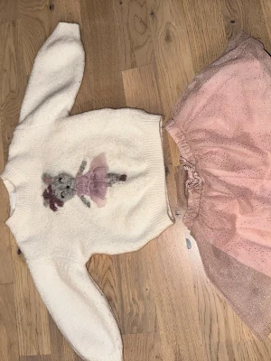 Sött set från Zara med ballerinatema - Sött set från Zara med ballerinatema. Supersött set från Zara med en mjuk, vit tröja med ballerina-motiv och en rosa tyllkjol med glitter. Perfekt för dig som gillar gulliga och lekfulla outfits. Tröjan har rund hals och långa ärmar, kjolen har resår i midjan för skön passform.