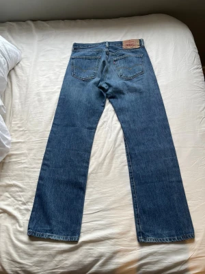 Levi's 501 - Klassiska blå jeans från Levi's med rak passform och fem fickor. Jeansen har en snygg tvättad look och är tillverkade i slitstark denim. Perfekta för dig som gillar tidlös stil och vill ha ett par jeans som funkar till allt. Modell: 501. Storlek: W32 L30. 