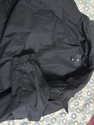 Svart jacka från H&M - Snygg svart bomberjacka från H&M med klassisk dragkedja framtill och praktiska fickor med knappdetaljer. Jackan har ribbade muddar vid ärmslut och krage för en clean look. Perfekt för dig som vill ha en enkel och stilren jacka.