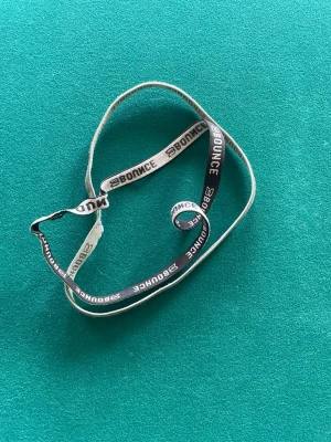 Svart och vit hårsnodd BOUNCE - Elastisk hårsnodd i svart och vitt med texten 'BOUNCE' tryckt längs hela bandet. Perfekt för att hålla håret på plats under träning eller till vardags. Tillverkad i stretchigt material som sitter bekvämt i håret.