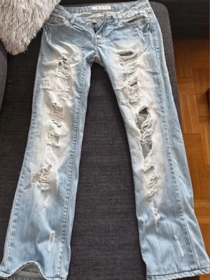 Ljusblå slitna jeans från Replay - Säljer ett par ljusblå jeans från Replay med kraftigt slitna och trasiga detaljer framtill. Jeansen har raka ben och klassisk femficksmodell. Materialet är denim i bomull och passformen är avslappnad. Perfekta för en edgy och trendig look. Står storlek M på lappen!