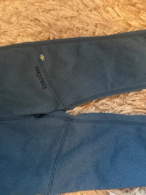 Blå mjukisbyxor från isbjörn - Mysiga blå underställsbyxor från isbjörn med svensk flagga broderad vid höften. Byxorna har ribbad struktur, resår i midjan och muddar vid bensluten. Perfekta för chill hemma eller som lager under andra kläder.