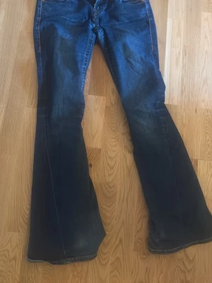 Blå bootcut jeans från True Religion - Säljer ett par mörkblå bootcut jeans från True Religion med klassiska kontrastsömmar och broderade bakfickor. Jeansen har låg midja och utsvängda ben. Har hål mellan benen men går absolut att sy❤️❤️Säljer eftersom de inte längre passar 