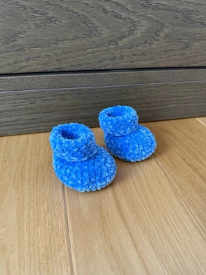 Blå fluffiga babytossor - Supersöta blå tofflor för baby i mjukt, fluffigt material. De har en rundad form och är perfekta för att hålla små fötter varma och gosiga. Passar perfekt för mysiga hemmadagar och är riktigt gulliga på de allra minsta. Handgjorda