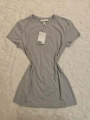 Ljusgrå basic t-shirt från H&M - En enkel och stilren ljusgrå t-shirt från H&M med rund halsringning och korta ärmar. T-shirten är gjord i mjuk bomull och har en normal passform som är perfekt för en avslappnad look. Perfekt att matcha med jeans eller shorts.