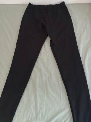 Svarta basic leggings - Ett par svarta leggings med hög midja och smal passform. De är stretchiga och mjuka, perfekta för en avslappnad stil. Klassisk modell utan synliga detaljer eller fickor. Passar till allt och är superenkla att matcha.