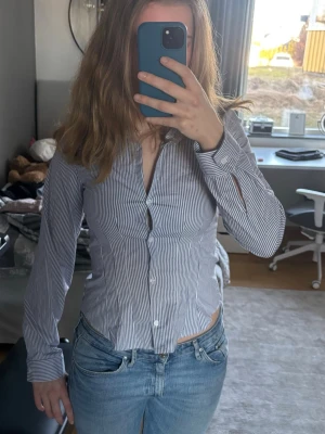 Blårandig skjorta - Snygg blårandig skjorta med smal passform och långa ärmar. Skjortan har klassisk krage och knäppning framtill. Perfekt till jeans för en clean och fräsch look. Säljs pga den var för liten. Den är egentligen storlek M men skulle mer säga storlek S.