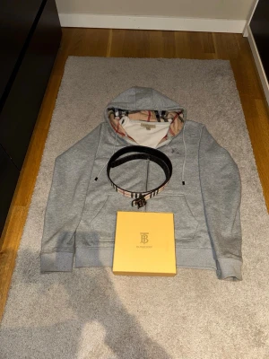 Hoodie & bälte inkl. box – mycket fint skick - Stilren grå zip-hoodie tillsammans med matchande bälte – en perfekt combo för en clean och trendig look. Hoodien har mjukt och bekvämt material med snygga detaljer, och bältet ger outfiten det lilla extra.  Mycket fint skick, sparsamt använd. Bältet säljs tillsammans med box och dustbag, vilket ger en extra lyxig känsla.  Pris för hoodie + bälte + box: 850 kr