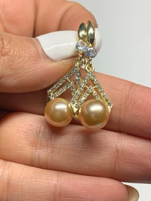 Guldörhängen med pärlor och stenar - Snygga örhängen i guldton med geometrisk design, dekorerade med gnistrande små stenar och stora champagnefärgade pärlor. Örhängena har även en klar sten upptill som ger extra bling. Perfekta för dig som vill sticka ut med en unik accessoar.