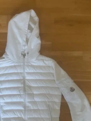 Vit dunjacka med huva från Moncler - Säljer en snygg vit dunjacka från Moncler med huva och quiltad design. Passar inte mig längre jag är 186 passar perfekt om du är 183 eller under. Perfekt passform runt armarna.