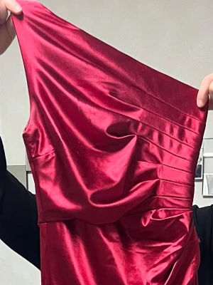 Vinröd långklänning i sammet - Säljer en elegant vinröd långklänning i mjuk sammet med oneshoulder-design. Klänningen har draperade detaljer upptill som ger en lyxig känsla och en smickrande siluett. Perfekt för dig som vill sticka ut med en klassisk och trendig look.