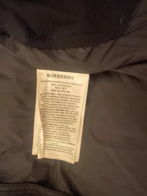Svart dunjacka från Burberry M - Snygg svart dunjacka som kan bli till en väst från Burberry i storlek M. Jackan har klassisk design med diskret logotypmärke på insidan och är fodrad med dun för extra värme. Perfekt för kalla vinterdagar och har en exklusiv känsla tack vare materialvalen.