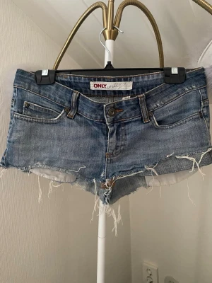 Blå jeansshorts från ONLY - Säljer ett par blå jeansshorts från ONLY med låg midja och råa, fransiga kanter. Klassisk femficksmodell med knapp och dragkedja framtill. Perfekta för sommaren och har en avslappnad, loose fit💕💕💕