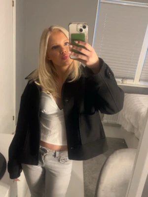 Svart kort jacka med knappar - Snygg svart jacka i kort modell med stora knappar framtill och krage. Jackan har en loose passform och är långärmad, perfekt att slänga över en outfit för en cool look.