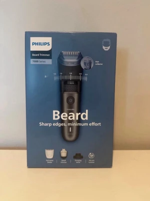 Philips skäggtrimmer 7000-serien - Philips skäggtrimmer 7000-serien med håruppsamlare, självslipande metallblad och precision på 0,2 mm. Trimmern är svart och silver, har flera kammar för olika längder och USB-laddning. Perfekt för att fixa skarpa kanter och detaljer.