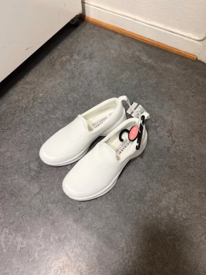 Vita slip-on sneakers från Primark - Fräscha vita slip-on sneakers från Primark med ovandel i textil och bekväm innersula i memory foam. Snygg minimalistisk design utan snörning, perfekt för en clean och enkel stil. Lätta att ta på och av, passar till många outfits.