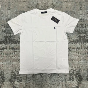 Vit t-shirt - Klassisk fin vit t-shirt med rund hals och korta ärmar. Liten mörkblå broderad logga på bröstet ger en clean och stilren look. Tillverkad i mjuk bomull för maximal komfort.