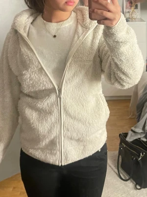 Vit fleecejacka  - Mysig vit fleece jacka med dragkedja och . Jackan har en fluffig, mjuk yta och en enkel, avslappnad passform. Perfekt för kalla dagar när du vill vara både varm och stilren. Jackan har fickor på sidorna och är helvit utan synligt märke.