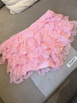 Ny i förpackning! Rosa volangshorts i spets - Supersöta korta rosa shorts med flera lager volanger i spets. Shortsen har elastisk midja och är perfekt för dig som gillar en lekfull och feminin stil. Passar till crop tops och sneakers för en trendig look.