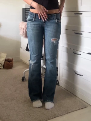 Diesel jeans - Säljer ett par blå bootcut jeans med slitningar och trasiga detaljer på låret och knät. Jeansen har klassisk femficksdesign och är tillverkade i denim. Perfekta för dig som gillar en avslappnad och trendig look.