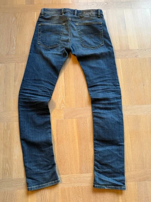 Mörkblå jeans från Diesel - Säljer ett par mörkblå jeans från Diesel med klassisk femficksdesign och snygga kontrastsömmar. Jeansen har raka ben och en patch med Diesel-logga bak i midjan. Materialet är mjukt denim som sitter skönt och passar till det mesta.