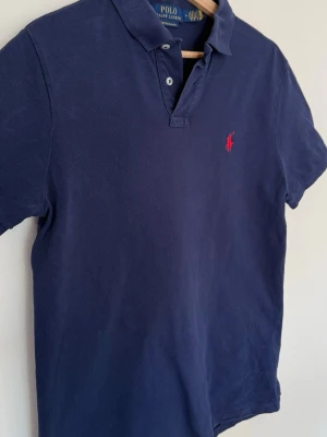 Marinblå pikétröja från Ralph Lauren - Klassisk marinblå pikétröja från Ralph Lauren med korta ärmar och röd broderad logga på bröstet. Använd >10 gånger. Utmärkt skick 🙌