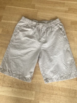 Beiga shorts med snörning - Snygga och luftiga beiga shorts i lin och bomull med elastisk midja och snörning framtill. Shortsen har två sidofickor. 