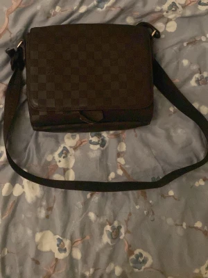 Louis Vuitton axelväska Damier Graphite - Snygg axelväska från Louis Vuitton i klassiska Damier Graphite-mönstret. Väskan är svart med gråa rutor och har justerbar axelrem. Tillverkad i canvas med läderdetaljer och har lockstängning framtill. Perfekt för dig som vill ha en stilren och trendig väska.PRIS KAN DISKUTERAS!
