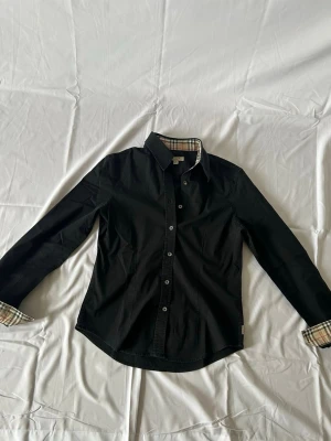 Svart Burberry skjorta med rutig detalj - Tja! Säljer nu denna svarta burberry skjortan i storlek M tjej. Men den passar även på killar som har storlek XS.                                                               Nypris: 5500kr.                                                       Säljs för: 599kr.                                                         Priset går att diskutera! Hör av er vid frågor eller funderingar! 