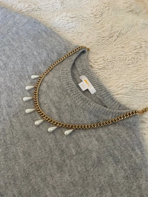 Guldhalsband med droppformade pärlor - Snyggt halsband i guldfärgad rostfritt med droppformade vita pärlor som hänger längs kedjan. Perfekt accessoar för att lyfta din outfit med en elegant touch. Kedjan har en klassisk design och pärlorna ger ett trendigt uttryck.