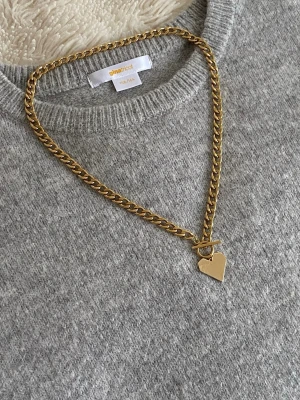 Guldigt halsband med hjärthänge - Snyggt halsband i guldfärgad rostfritt. Kedjan är chunky och har ett geometriskt hjärthänge samt ett dekorativt T-lås framtill. Perfekt accessoar för att lyfta din outfit med en trendig touch.