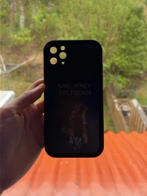 Svart mobilskal med textmotiv - Snyggt svart mobilskal med trycket 'MAKE MONEY NOT FRIENDS' och en bild på en person med pengar. Skalet har öppningar för tre kameror och blixt, och är gjort i ett tåligt material som skyddar mobilen. Perfekt för dig som vill ha en cool och edgy stil.