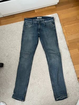 Blå Replay jeans W30 L34 - Snygga blå slim Replay Jeans med klassisk femficksdesign och dragkedjegylf. Jeansen har en lätt tvättad look och diskreta slitningar på benen. Perfekta för en avslappnad och trendig stil.