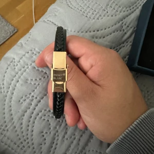 Svart skinn Mont Blanc armband - Mont blanc armband i skinn med detaljer i guld.                                                            Storlek 21 cm.  Skick 10/10 oanvänd. Armbandet fick jag och säljer då den aldrig använts. Billigt pris p.ga. att jag inte har kvitto. Liknande armband går för 3000-4000 kr. 