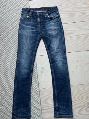 Mörkblå jeans från Nudie Jeans - Snygga mörkblå jeans från Nudie Jeans med klassisk femficksdesign och orangea sömmar på bakfickorna. Jeansen har en smal passform och är tillverkade i denim med lätt slitning för en cool look.