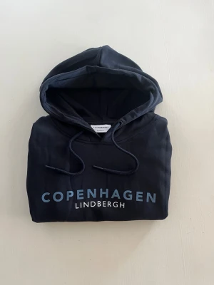 Hoodie från Lindbergh - Mörkblå hoodie från Lindbergh med trycket 'Copenhagen'. Tröjan är helt oanvänd, kostar 799kr ny —> säljer för 449kr. Hör av dig om du har någon fundering.