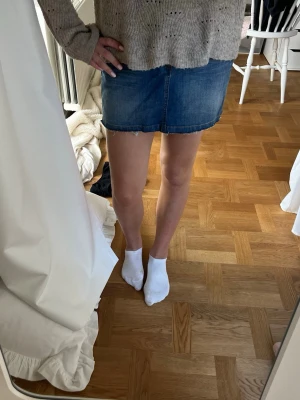 Blå jeanskjol från Lindex - Snygg blå jeanskjol från Lindex i klassisk femficksmodell. Kjolen är kort och har en rak passform med knapp och dragkedja framtill. Perfekt att matcha med en stickad tröja eller t-shirt.