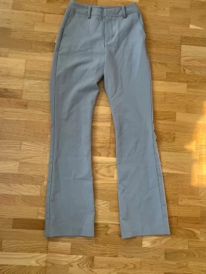 Grå kostymbyxor från BikBok - Snygga grå kostymbyxor från BikBok i klassisk rak modell med pressveck och hällor för bälte. Byxorna har dragkedja och knapp framtill. Aldrig använda och i modellen ”Wilma”
