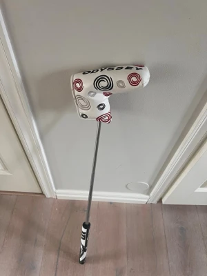 Odyssey O-Works golfputter (nytt grepp) (vänster) - Säljer en Odyssey O-Works golfputter med svart klubbhuvud och vit headcover med röda och svarta spiralmönster. Skaftet är i metall och greppet har svartvita detaljer. Perfekt för dig som vill förbättra din puttning på greenen. Längden är 34 inch. 