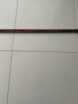 Bauer Pulse hockeyklubba svart/röd - Säljer en Bauer Pulse hockeyklubba i svart med röda detaljer. Klubban har en sportig design och är tillverkad i ett lätt material som passar perfekt för dig som gillar hockey. Snygg och funktionell för både träning och match. Det är en shl spelares klubba
