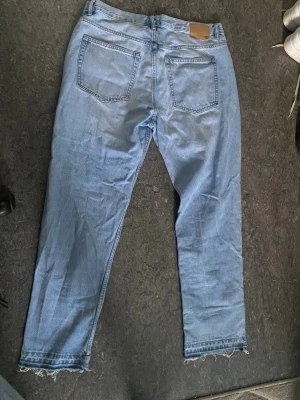 flared jeans  - Ljusblå jeans med rak passform och rå, fransad kant nedtill. Klassisk femficksmodell med bälteshällor och knappgylf. Perfekta för en avslappnad och trendig stil.