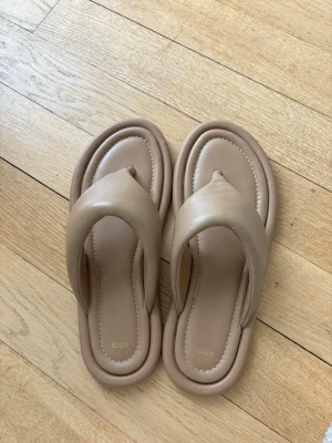 Beige chunky sandaler från Mango - Trendiga chunky sandaler från Mango i beige färg. Modellen har breda remmar och tårem, samt en vadderad sula för extra komfort. Tillverkade i ett mjukt, läderliknande material med modern design och rundad form.