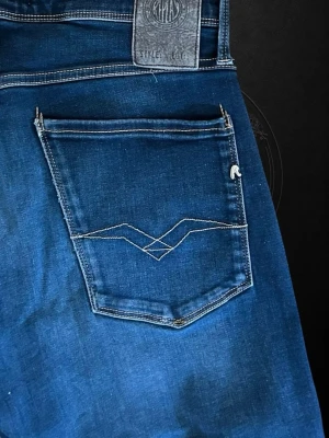  Replay Anbass - Snygga blå jeans från Replay med klassisk femficksdesign och coola detaljer på bakfickan. Jeansen har en slim fit passform och är gjorda i stretchigt denim-material som sitter skönt och följer kroppen. Perfekt för dig som gillar stilrena och moderna jeans.