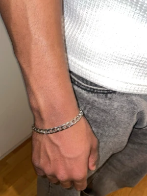 Silverfärgat kedjearmband - Stilrent armband i silverfärg med breda, platta länkar och karbinlås. Perfekt accessoar för en modern look. Armbandet har en klassisk kedjedesign och är tillverkat i metall.